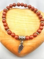 A RED JASPER BRACELET WITH FEATHER with leaf and silver charm.