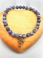 UN BRACCIALE DI SODALITE DA 6 MM CON CIONDOLO CHIAVE con una pietra blu e una chiave d'argento.