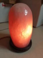 UNA LAMPADA QUARZO ROSA LEVIGATA 2/3 KG con sopra un sasso rosa.