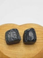 Due pietre nere TORMALINA NERA SEMI BURATTATA sopra una tavola di legno.