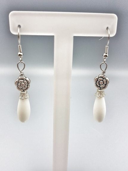 A pair of earrings WHITE AGATE AND FLOWER EARRINGS on a stand.