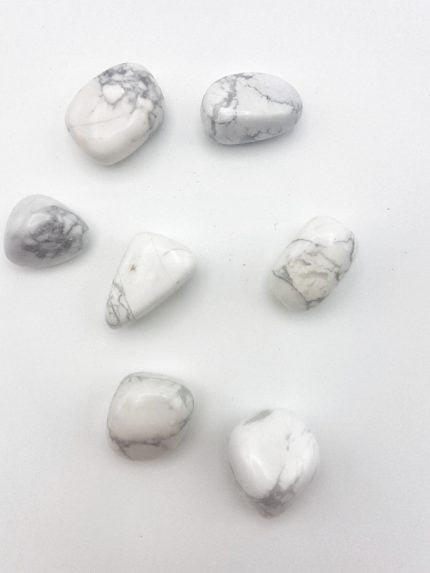 A group of white HOWLITE tumbled stones on a white surface.