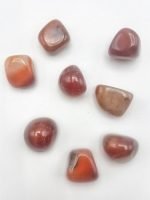 A collection of red stones of CARNELIAN TUMBLED on a white surface.