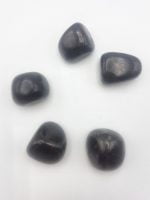 A group of black stones arranged on a white surface, resembling Tumbled Shungite.