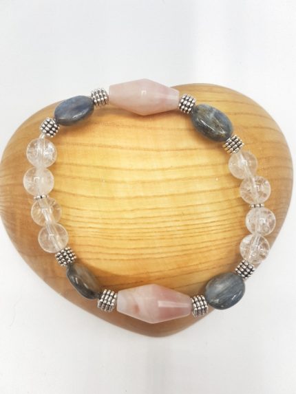 A PINK OPAL, KYANITE AND ROCK CRYSTAL BRACELET with pink opal and crystals on a wooden base.