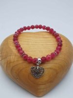 A RUBY JADE BRACELET with a heart-shaped pendant on a wooden base.