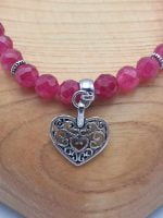 A jade bracelet with a ruby heart-shaped pendant dangling from it.
