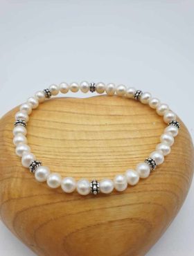 Un bracciale di perle bianche su un cuore di legno.