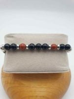 A MEN'S BRACELET WITH BLACK ONYX AND RED JASPER WITH BLACK LEATHER on top of a wooden box.