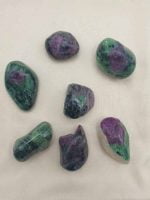 A cluster of green Zoisite stones and purple Ruby Tumbled stones arranged on a white cloth.  [ZOISITE RUBINO BURATTATA]
