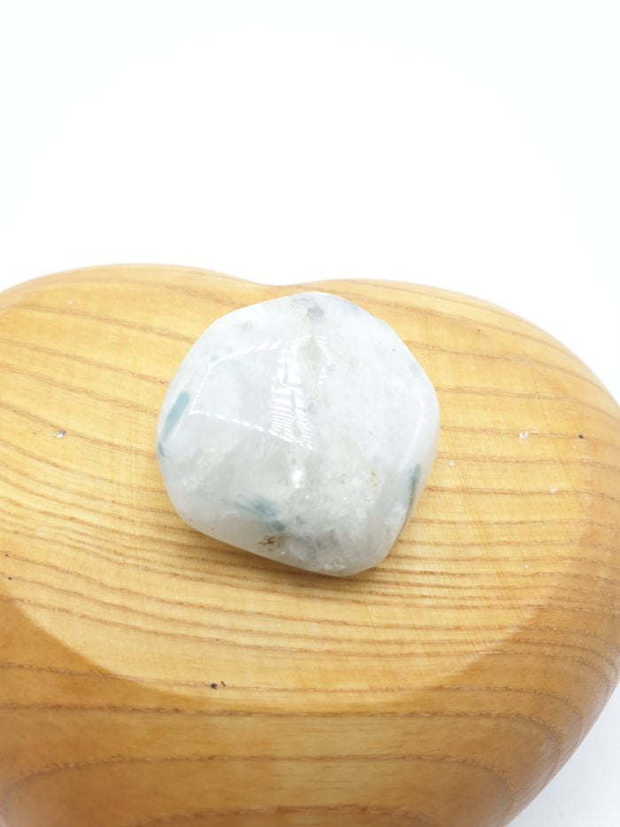 Una pietra PIETRA DI LUNA BIANCA BURATTATA bianca appoggiata su un cuore di legno.