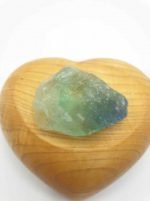 A green RAW RAINBOW FLUORITE sits on top of a wooden heart.