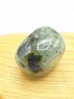 A green **TUMBLED PREHNITE** stone resting on a wooden board.