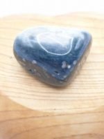 UN DIASPRO OCEANO BURATTATO sasso a forma di cuore appoggiato su una tavola di legno.