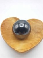 A black ball on a wooden plate in the shape of a heart, with the SHUNGITE SPHERE 4 CM.