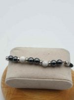 A MEN'S BRACELET WITH HEMATITE, WHITE HOWLITE AND BLACK LEATHER CORD, displayed on a wooden box.