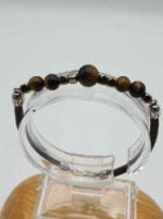 A BRACCIALE UOMO CON OCCHIO DI TIGRE, EMATITE E CORDINO CUOIO MARRONE (braccialetto da uomo con perline occhio di tigre, ematite e cordino di cuoio marrone) su supporto di legno.