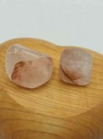 Two stones of HEMATOID QUARTZ WITH TRACES OF TUMBLED LITHIUM on a wooden surface.