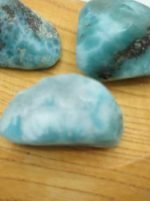 Three pieces of Larimar Tumbled on a wooden table.