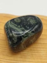 Una pietra di diaspro verde che ricorda una NEBULA BURATTATA su una tavola di legno.