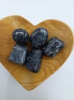 A wooden bowl in the shape of a heart with blue stones LARVIKITE TUMBLED inside.