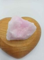 A RAW PINK ARAGONITE stone resting on a wooden heart.