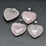 Three ROSE QUARTZ HEART PENDANT IN PLATED BRASS on a black surface, embellished with bronzed accents.