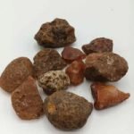 A collection of raw red carnelian stones on a white surface.