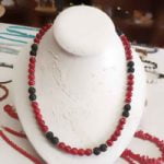 A BAMBOO CORAL AND BLACK LAVA STONE NECKLACE with red and black coral beads on mannequin.