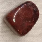 A red PIERTERSITE STONE TUMBLED on a white surface.