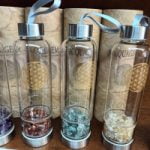 A collection of AMETHYST ELIXIR AQUAGEM BOTTLES fills with stones and crystals.